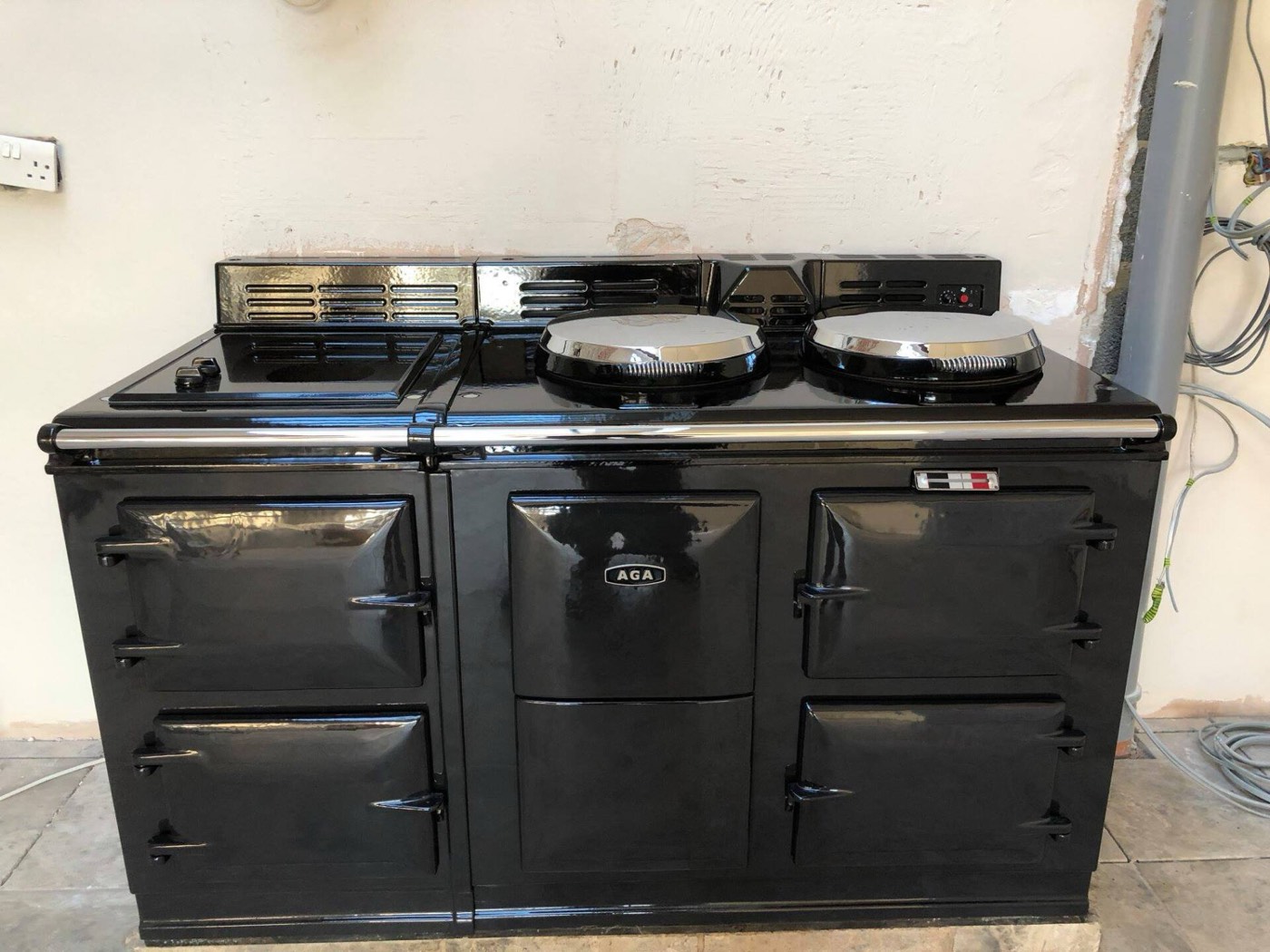 A gleaming black four-oven Aga with polished chrome hotplate lids, against a freshly plastered wall